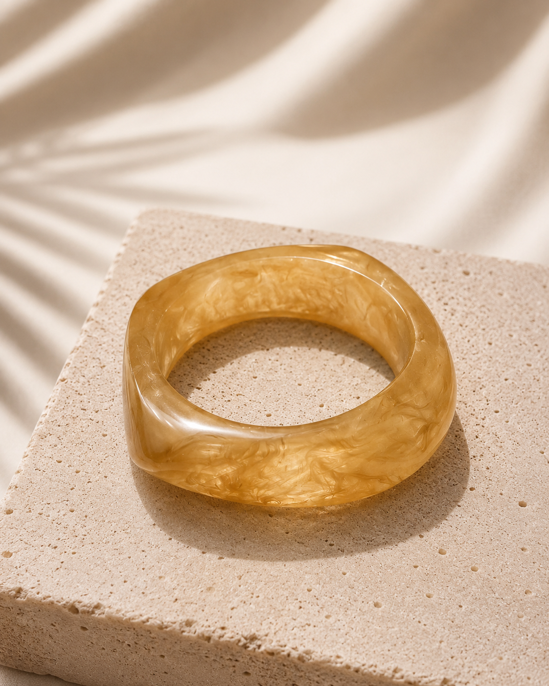 Yellow-brown bangle on a textured beige surface with soft shadows